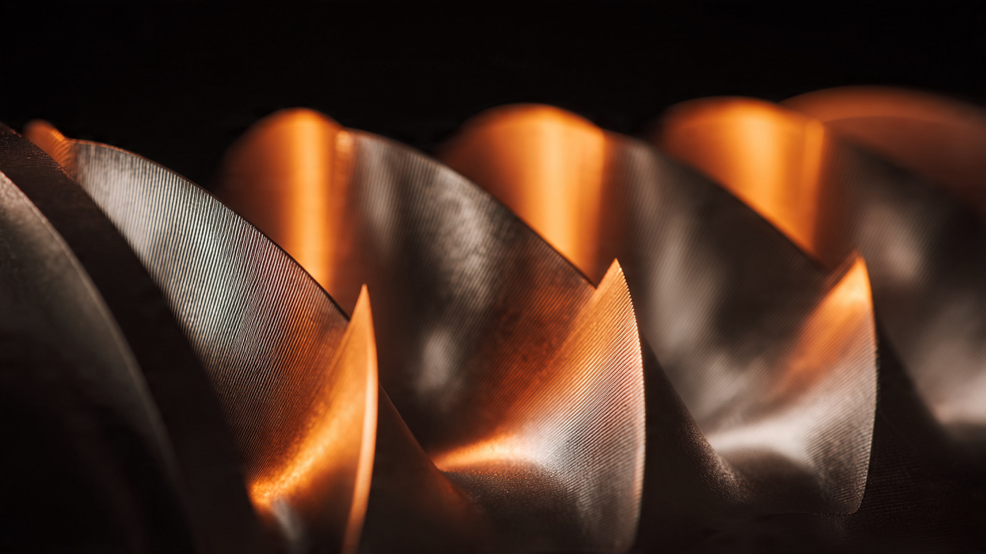Close-up macro photograph of supercharger rotor assembly showing four helically twisted aluminum lobes with warm directional lighting revealing precision machining surfaces