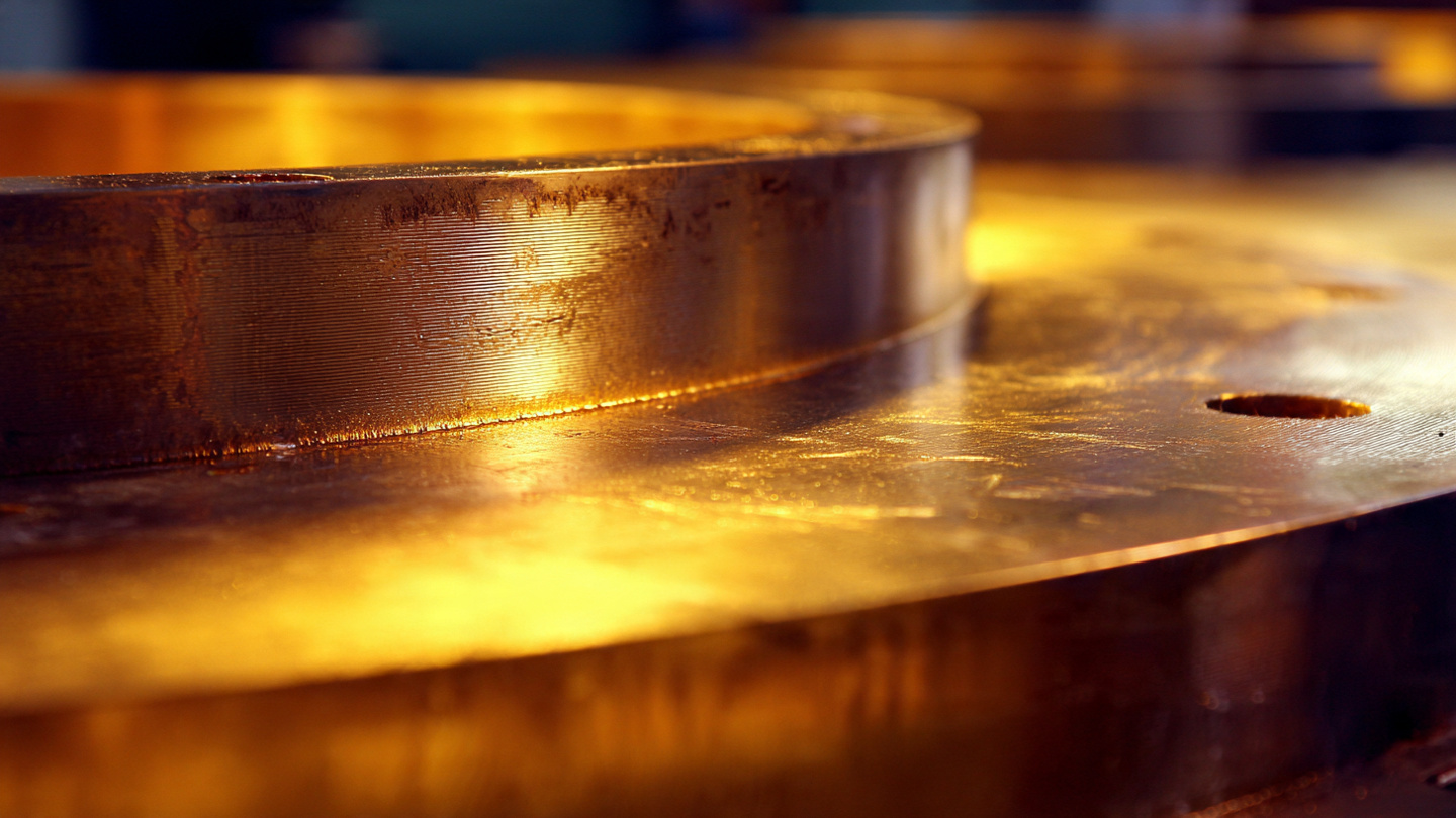Macro photograph of a large polished aluminum gigacasting underbody section showing smooth die-cast surface with visible gate marks under warm workshop lighting