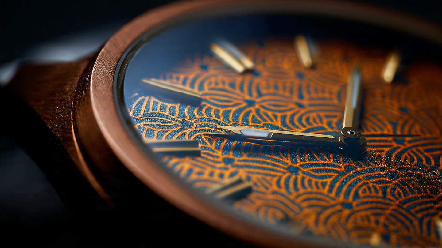 Macro photograph of a metallic lattice watch dial with geometric interlocking ridges and microscopic perforations under warm amber directional lighting