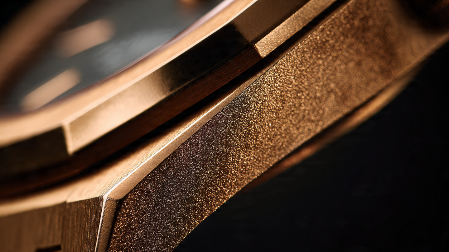 Macro photograph of a polished gold watch case and bezel under warm amber directional lighting showing the distinctive warm tone and satin-finished surface of Hublot Magic Gold cermet alloy