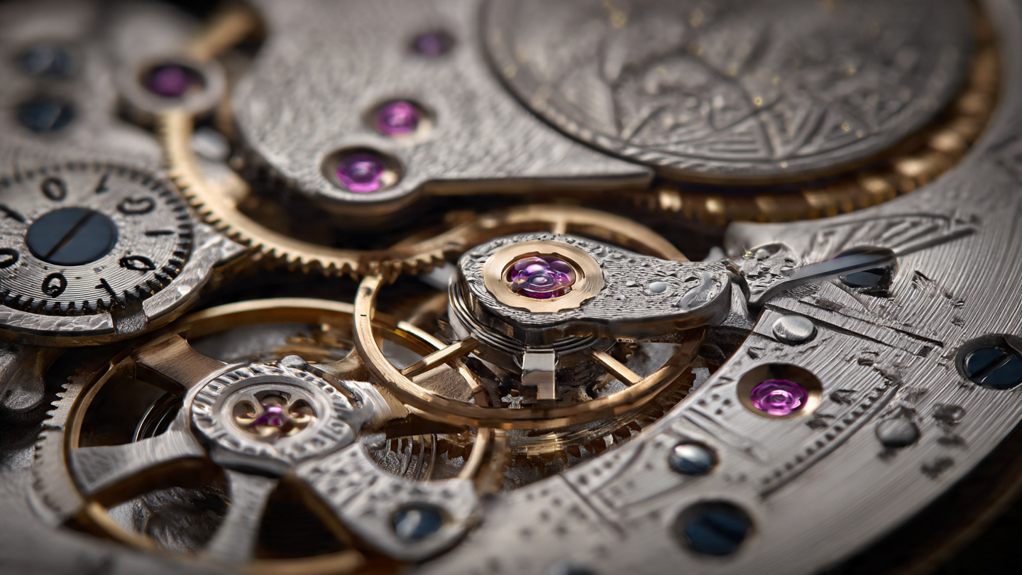 Macro photograph of a mechanical watch movement showing numeral discs visible through apertures, with a German silver bridge and constant-force mechanism visible beneath
