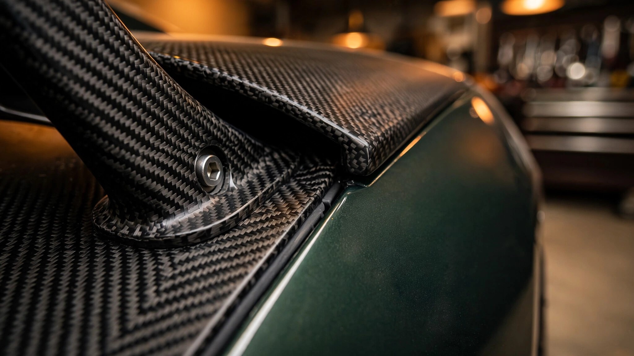 Close-up of sculpted carbon fiber bodywork showing the woven pre-preg composite weave pattern in warm amber studio lighting