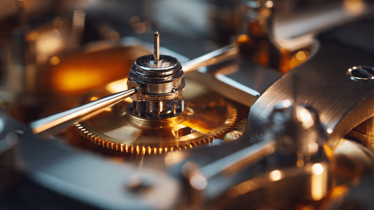 Macro photograph of a minute repeater striking mechanism showing wire gongs and polished steel hammers under warm directional lighting