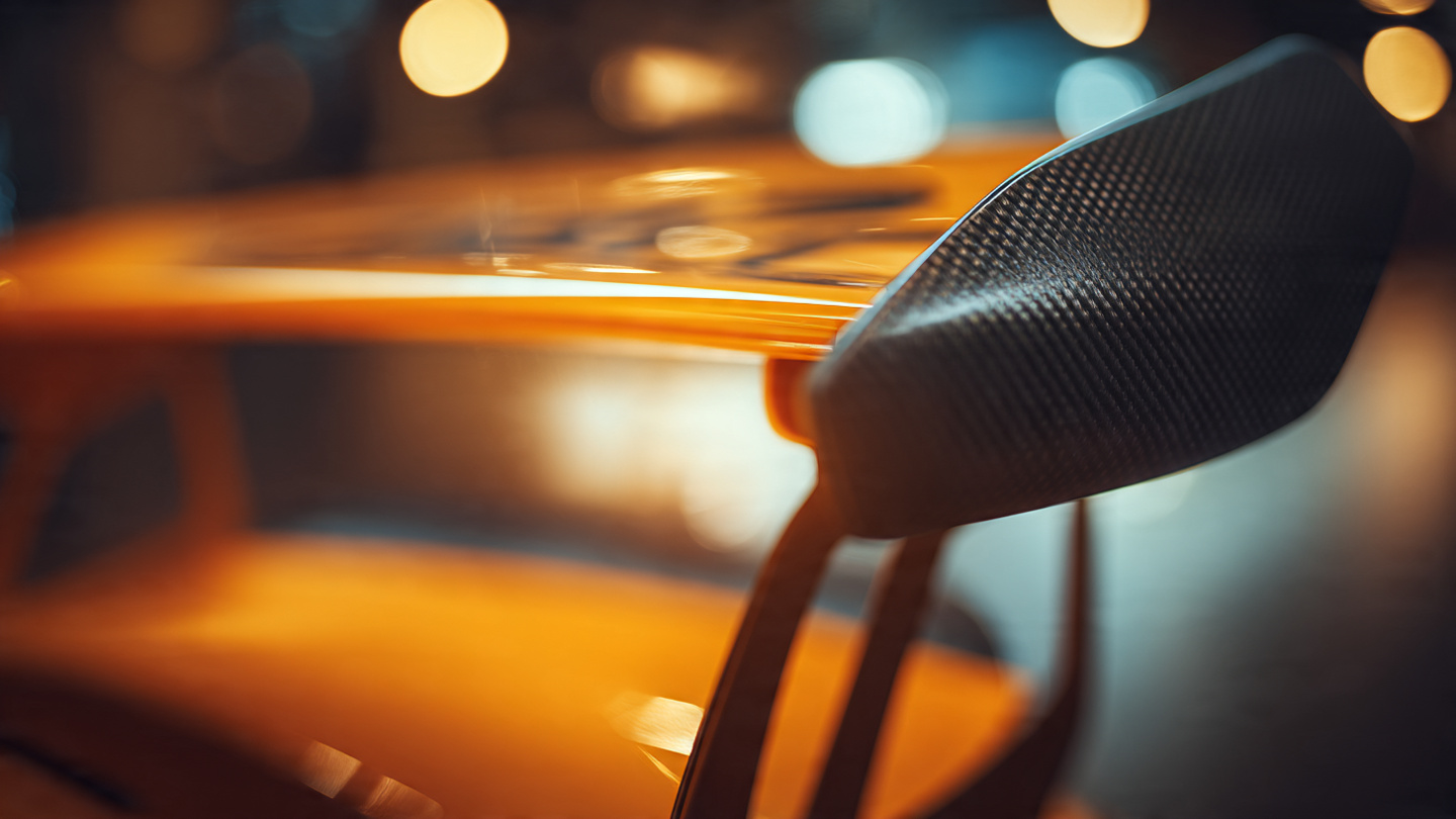 Close-up of Porsche GT3 RS rear wing carbon fiber swan-neck mount and active aerodynamic elements under warm lighting