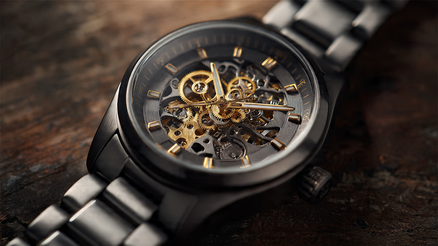 Macro photograph of a gray plasma ceramic watch case with skeletonized movement showing gold-toned gears under warm amber lighting