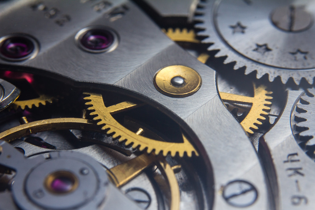 Split composition: watch movement macro and engine bay detail, warm amber tones